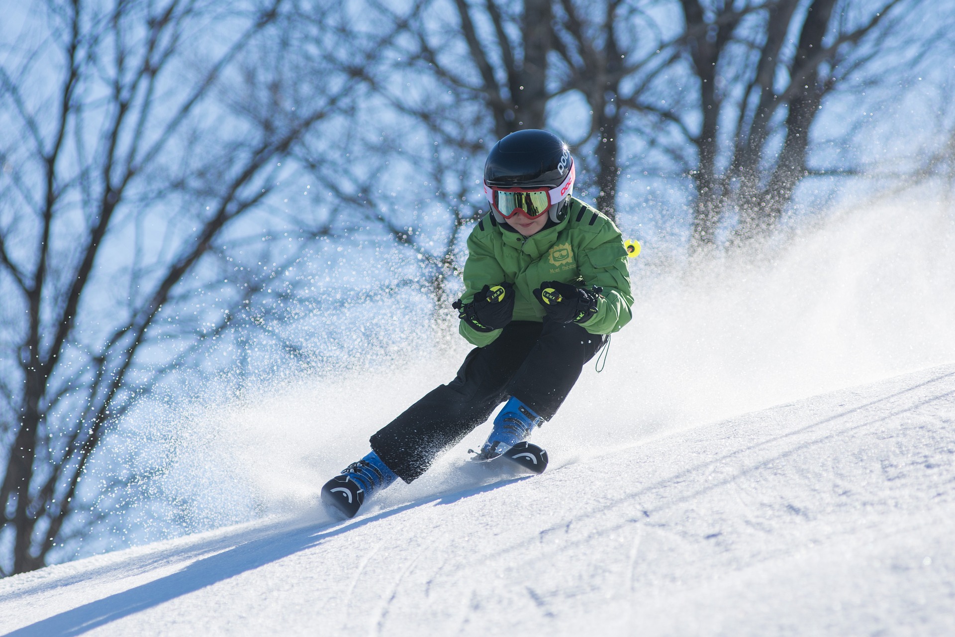kid with green jacket skiing down a slope.